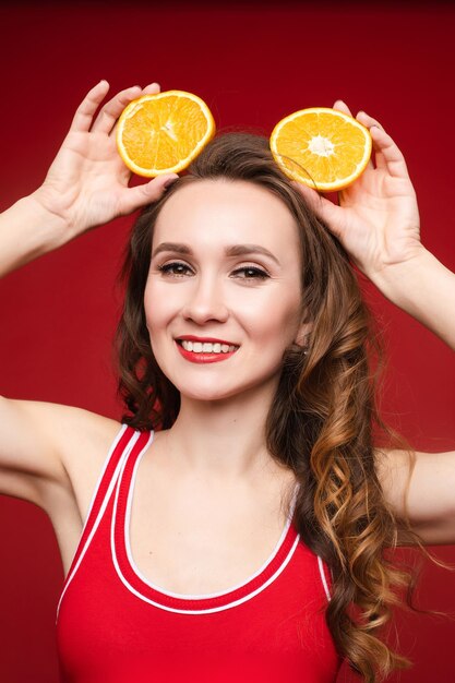Hermosa mujer en traje de baño rojo con maquillaje brillante y labios rojos con rodajas de naranja alegría de brillo de verano