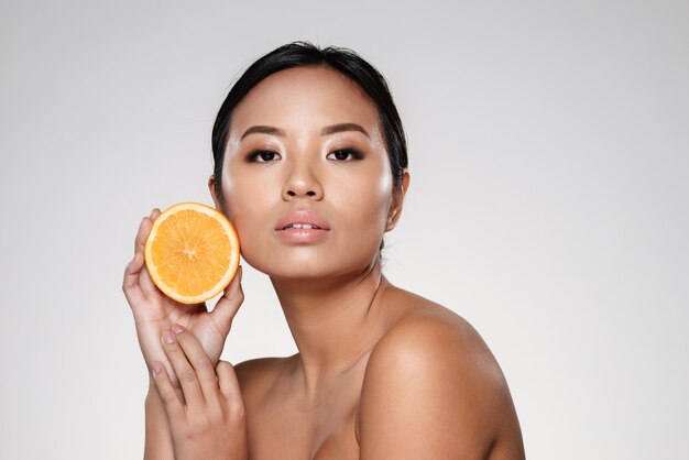 Hermosa mujer tranquila mostrando rodaja de naranja y mirando a cámara