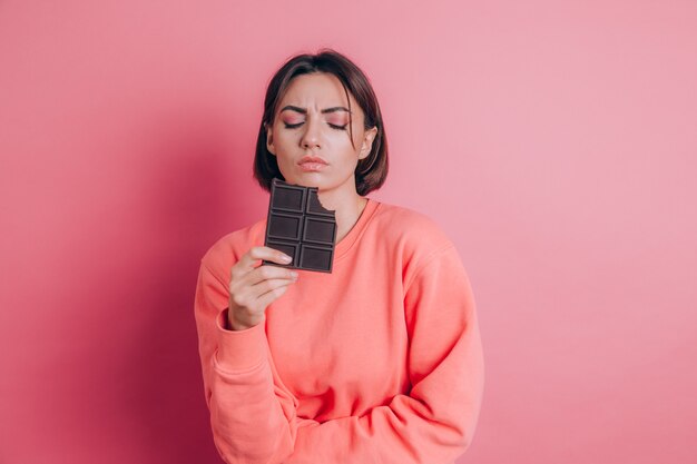 Hermosa mujer triste con dolor abdominal con barra de chocolate sobre fondo rosa y maquillaje brillante