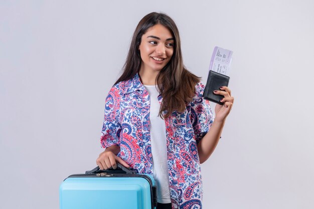 Hermosa mujer turista con maleta de viaje y pasaporte con boletos mirando a un lado con una sonrisa en la cara feliz y positivo concepto de viaje de pie