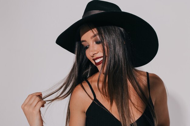 hermosa mujer usa maquillaje de halloween, vestida con traje negro, corona oscura, se ve con expresión aterradora, aislada sobre una pared gris