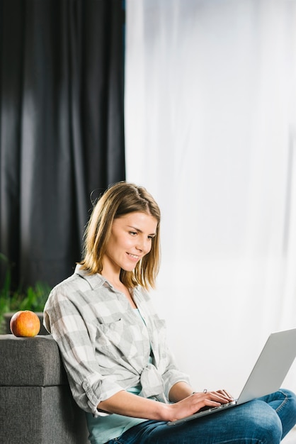 Hermosa mujer usando laptop cerca de sofá