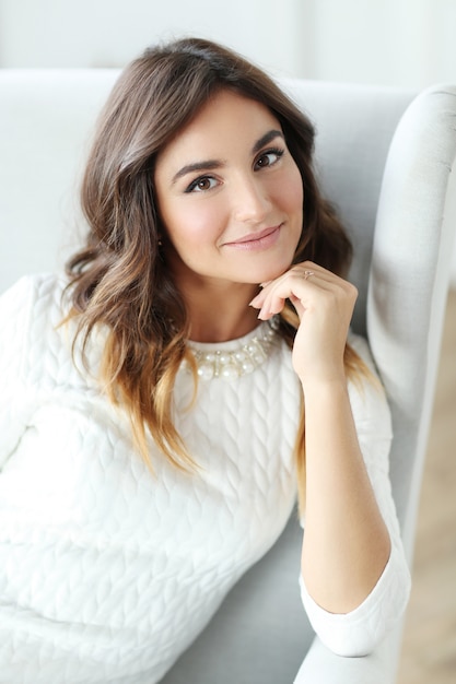 Hermosa mujer vestida de blanco y sentada en un sillón blanco