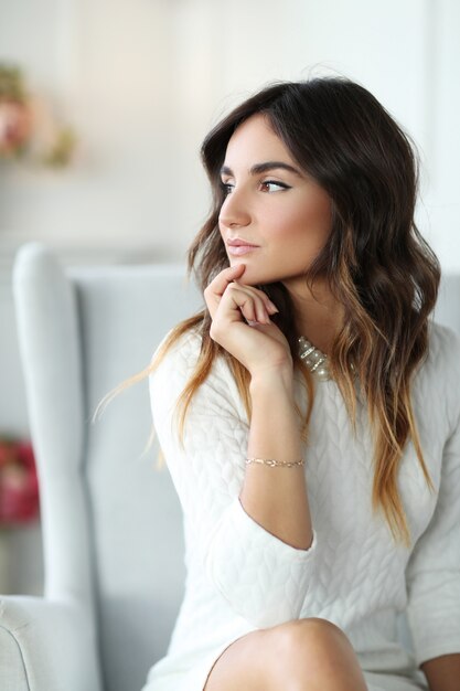 Hermosa mujer vestida de blanco y sentada en un sillón blanco