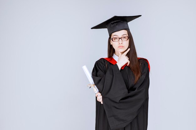 Hermosa mujer vestida con diploma pensando. Foto de alta calidad