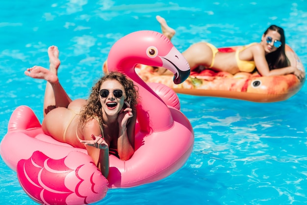 Hermosa mujer, vestida con traje de baño, acostada sobre un colchón de aire flamingo rosa en una piscina de agua azul, verano.