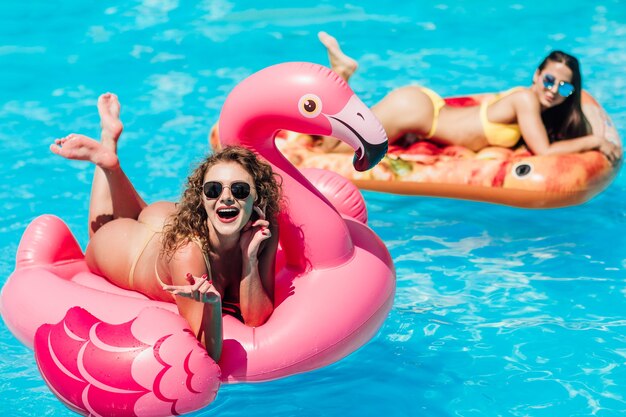 Hermosa mujer, vestida con traje de baño, acostada sobre un colchón de aire flamingo rosa en una piscina de agua azul, verano.