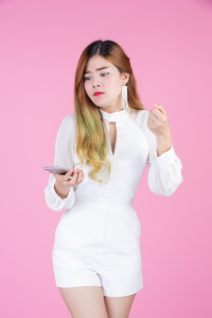 Una hermosa mujer vestida con un vestido blanco, mostrando el teléfono y las emociones faciales.