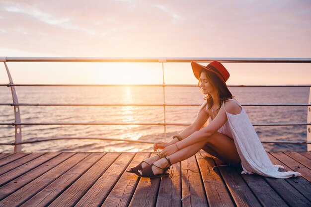 Hermosa mujer en vestido blanco sentada junto al mar al amanecer en estado de ánimo romántico