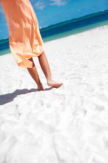 Hermosa mujer en vestido caminando cerca de la playa del océano en día de verano en arena blanca