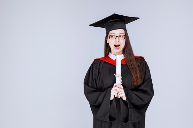 Hermosa mujer en vestido con diploma sintiéndose feliz. Foto de alta calidad