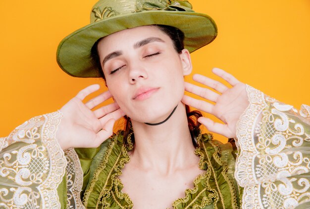 Hermosa mujer en vestido renacentista y sombrero con los ojos cerrados con expresión soñadora en naranja