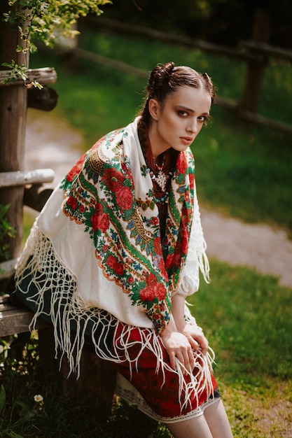 Foto gratuita hermosa mujer con un vestido tradicional bordado está sentado en el banco y mirando