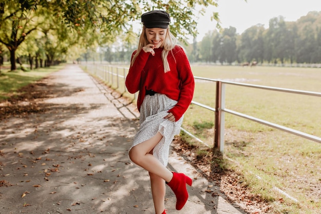 Hermosa mujer en zapatos rojos de moda posando en el camino del parque Chica rubia divirtiéndose al aire libre