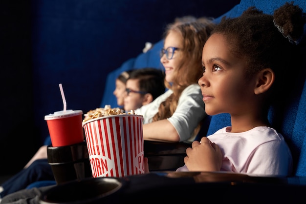 Hermosa niña africana con peinado divertido viendo películas en el cine