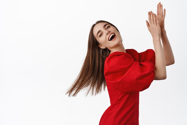 Hermosa niña bailando flamenco, riendo y disfrutando de la música y los bailes, aplaudir al ritmo, sonriendo natural, posando en vestido rojo sobre blanco