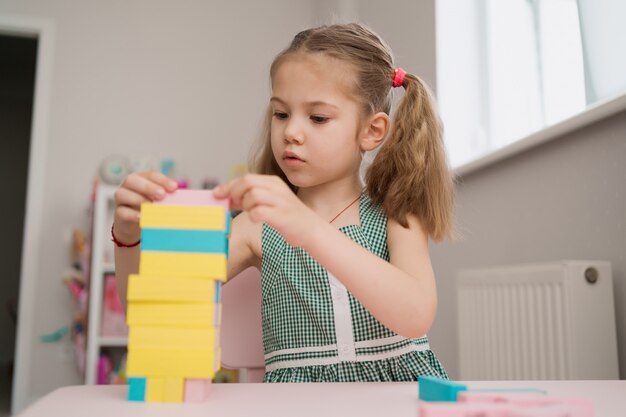 Hermosa niña caucásica jugando con bloques multicolores de madera