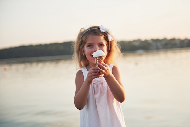 Una hermosa niña come un helado cerca del agua