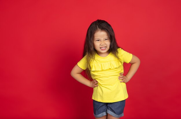 Hermosa niña emocional aislada en el espacio rojo. Retrato de medio cuerpo de niño feliz mostrando un gesto y apuntando hacia arriba. Concepto de expresión facial, emociones humanas, infancia.