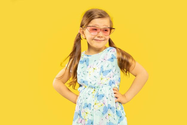 Hermosa niña emocional aislada. retrato de niño feliz de pie y con un vestido y gafas de sol rojas. Concepto de verano, emociones humanas, infancia.