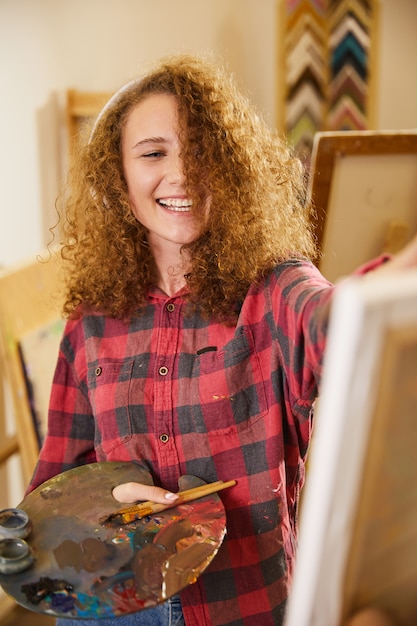 Hermosa niña escucha música a través de auriculares, ríe y dibuja una pintura