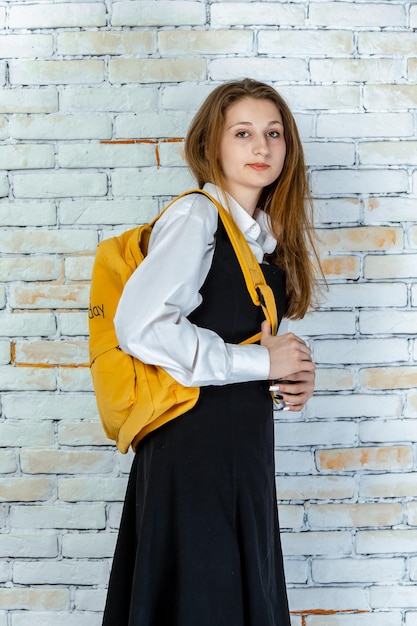 Hermosa niña de la escuela en un uniforme se encuentra en fondo blanco.