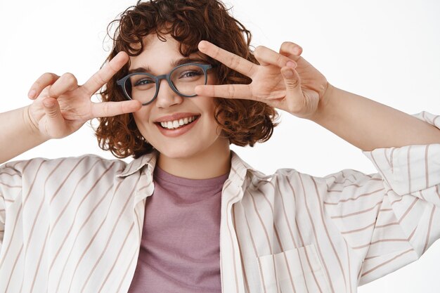 hermosa niña feliz con dientes blancos, sonrisa alegre y signo de paz kawaii en v cerca de los ojos, de pie positivo y alegre en blanco