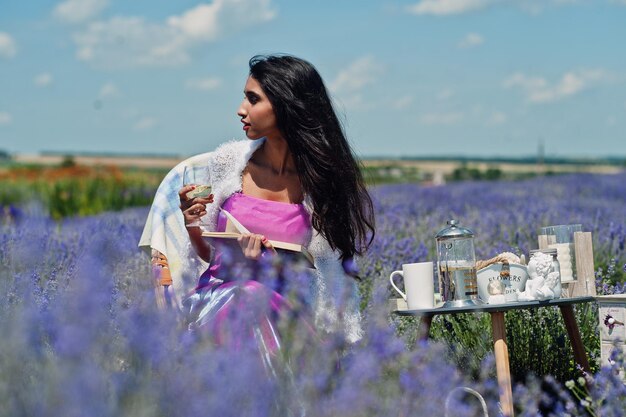 Hermosa niña india usa vestido tradicional saree india sentada en un campo de lavanda púrpura con decoración