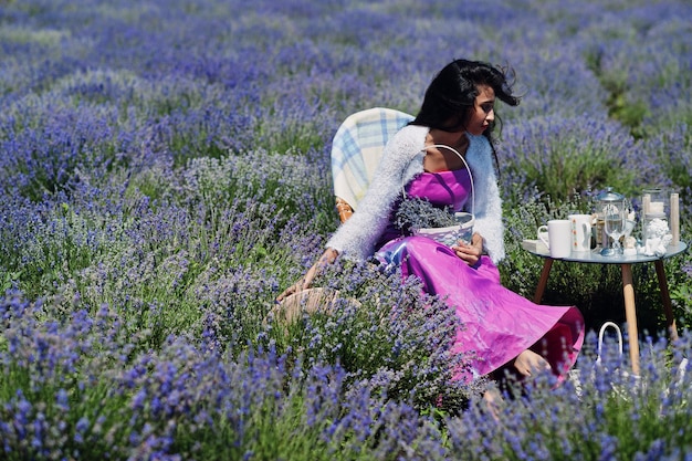 Hermosa niña india usa vestido tradicional saree india sentada en un campo de lavanda púrpura con decoración