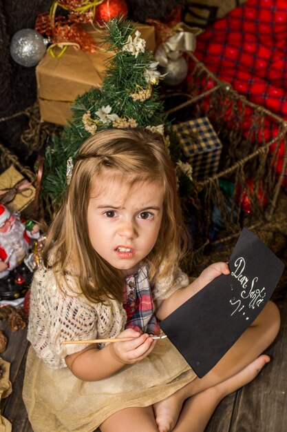 Hermosa niña linda escribe carta a Santa cerca de la decoración de Navidad en el piso de madera