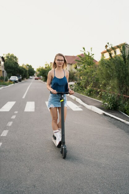 Hermosa niña montando un scooter eléctrico en el verano en la calle