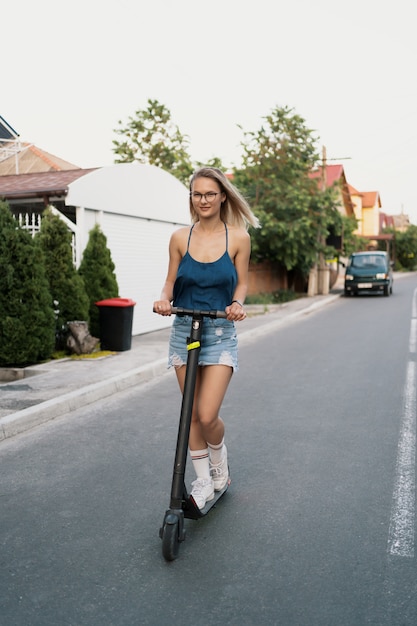 Hermosa niña montando un scooter eléctrico en el verano en la calle