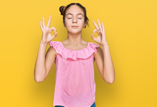 Hermosa niña morena con pantalones rosa de verano se relaja y sonríe con los ojos cerrados haciendo gestos de meditación con los dedos. concepto de yoga