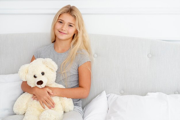 Hermosa niña sentada en la cama con su osito de peluche