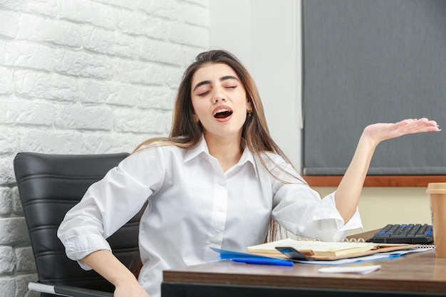 Una hermosa niña sentada detrás del escritorio y levantó la mano Foto de alta calidad