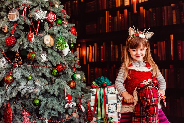 La hermosa niña sentada en el hobbyhorse cerca del árbol de Navidad