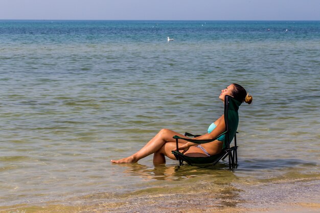 hermosa niña sentada sola en el mar, bonito bronceado