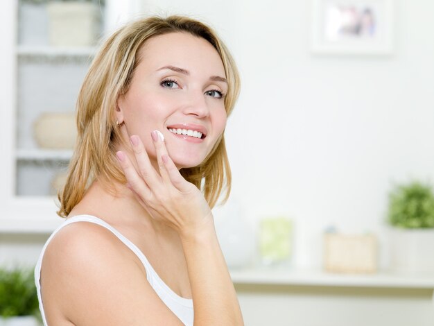 Hermosa niña sonriente aplicando crema en la cara