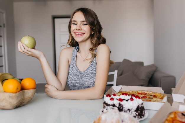 Hermosa niña sonriente comiendo frutas frescas por la mañana. Retrato interior de la encantadora modelo femenina disfrutando de un desayuno saludable foodfor.