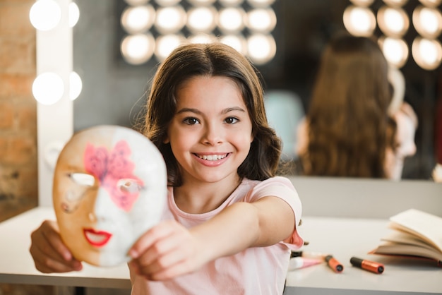 Hermosa niña sonriente de pie en el backstage mostrando mascarilla