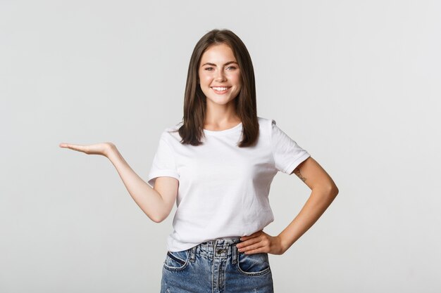 Hermosa niña sonriente presenta algo, sosteniendo en la mano.