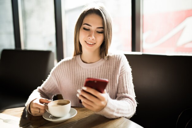 Hermosa niña sonriente con su teléfono móvil en la cafetería durante el almuerzo de freno de café todos los días