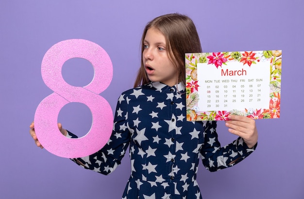 Hermosa niña sorprendida en el día de la mujer feliz sosteniendo el calendario mirando el número ocho en su mano