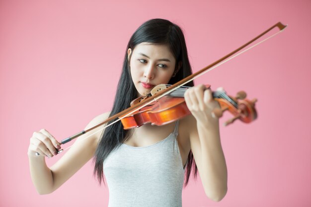 hermosa niña tocando el violín sobre fondo rosa