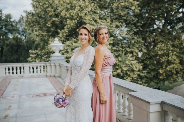 Hermosa novia con una dama de honor en un balcón posando para la sesión de fotos de la boda