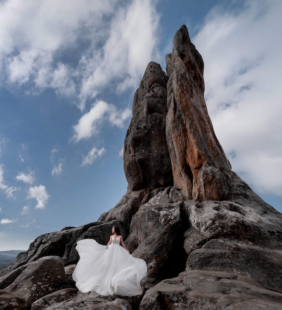 Hermosa novia está de pie sobre la roca cerca del alto acantilado en el día claro con cielo azul