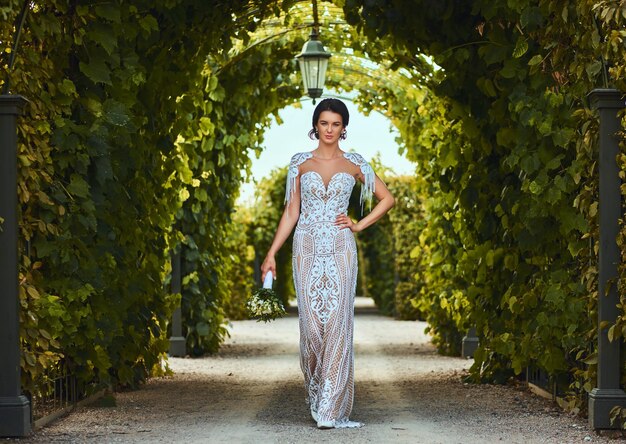 Hermosa novia feliz con un hermoso vestido sosteniendo el ramo de novia y caminando en el jardín.