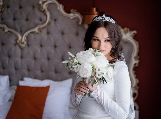 Hermosa novia en la habitación del hotel con ramo de novia hecho de eustomas y peonías blancas