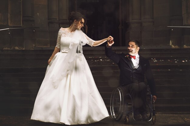 Hermosa novia y el novio en la silla de ruedas bailan antes de la antigua iglesia católica