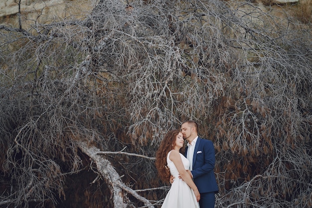 hermosa novia de pelo largo joven en vestido blanco con su joven esposo cerca de las ramas